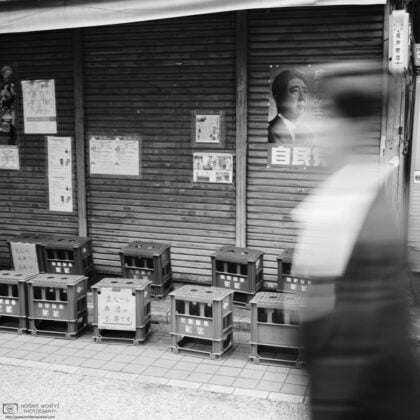 At Yanaka Ginza in Tokyo, Japan, a woman is walking past a shop that is decorated with a poster of Shinzo Abe.